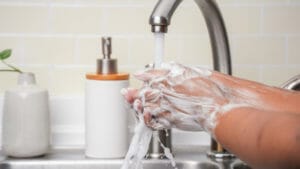 Two hands washing under a sink faucet.